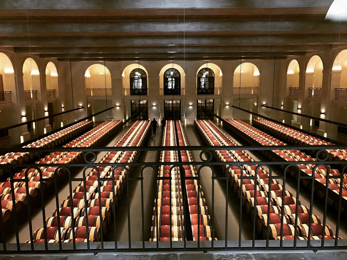 A barrel hall, rows of oak casks under stone arches